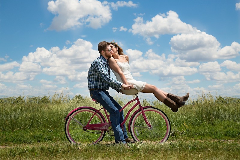 Homme heureux sur un vélo avec sa femme assise sur le guidon et l'embrassant